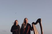 zwei Frauen mit einer Harfe, im Hintergrund fliegt ein Vogel am Himmel