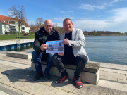 Herr Blohm und Herr Gottschalk sitzen mit einem Bild von den Sitzhockern am Nordufer des Uckersees