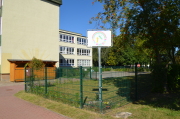 Im Vordergrund steht das Logo mit Regenbogenfarben und 2 Kindern und im Hintergrund der Kindergarten