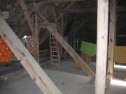 Dachboden mit Balken, nicht gedämmt, mit Leinen auf denen Decken hängen, eine Holzleiter lehnt am Balken