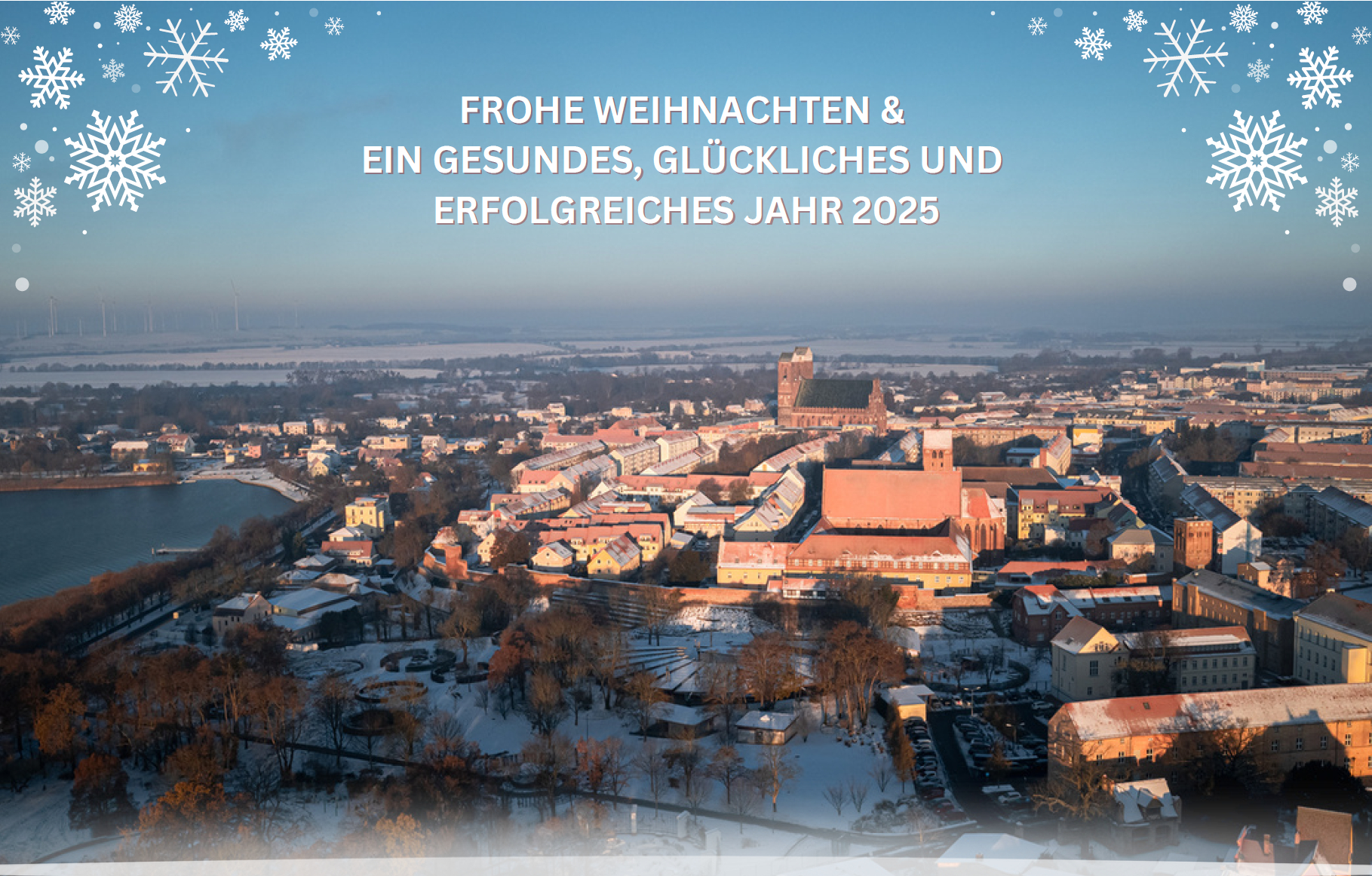 Luftbild von Prenzlau vom Seepark zur Marienkirche mit Schnee bedeckt, an den Ecken gezeichnete Schneefloken und in der Mitte FROHE WEIHNACHTEN & EIN GESUNDES, GLÜCKLICHES UND ERFOLGREICHES JAHR 2025